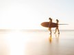 Zwei Freundinnen die mit ihren Surfbrettern über den Strand laufen