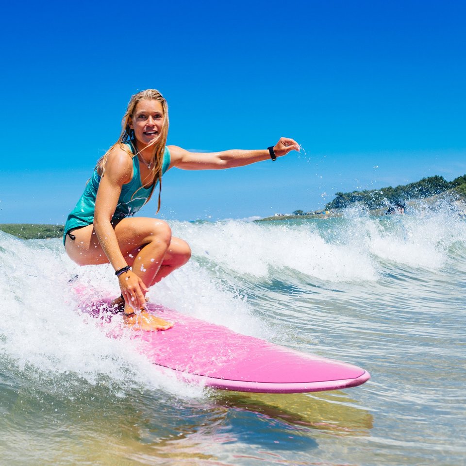 Frau in Badeanzug surft Welle auf pinkem Surfboard im Surfcamp Spanien
