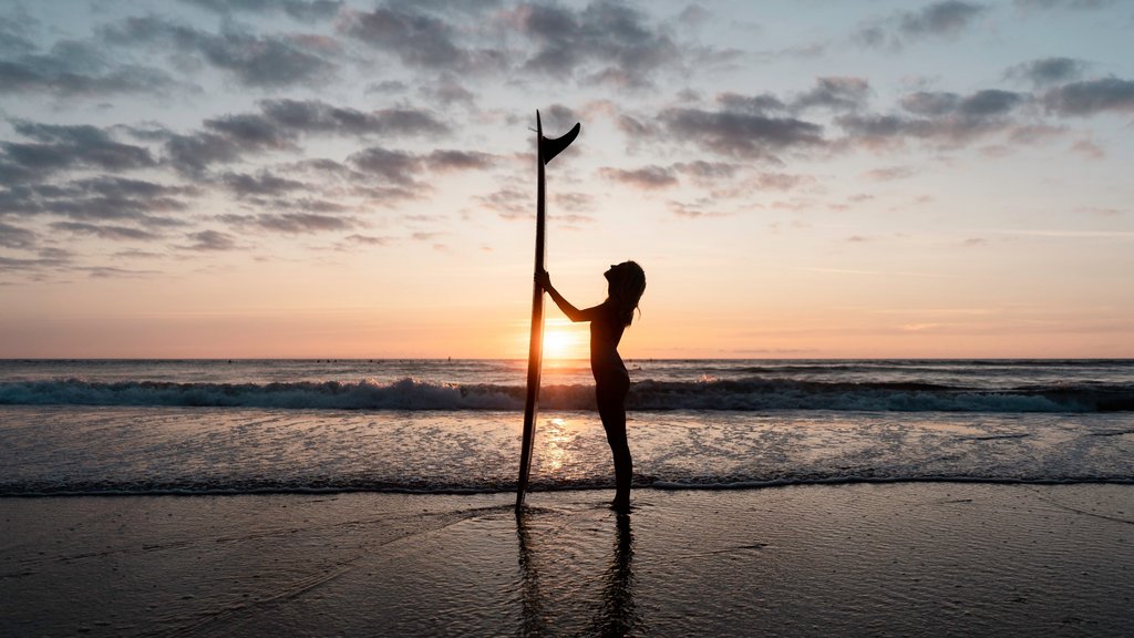 Eine Frau steht im Sonnenuntergang mit einem Surfbrett am Strand 