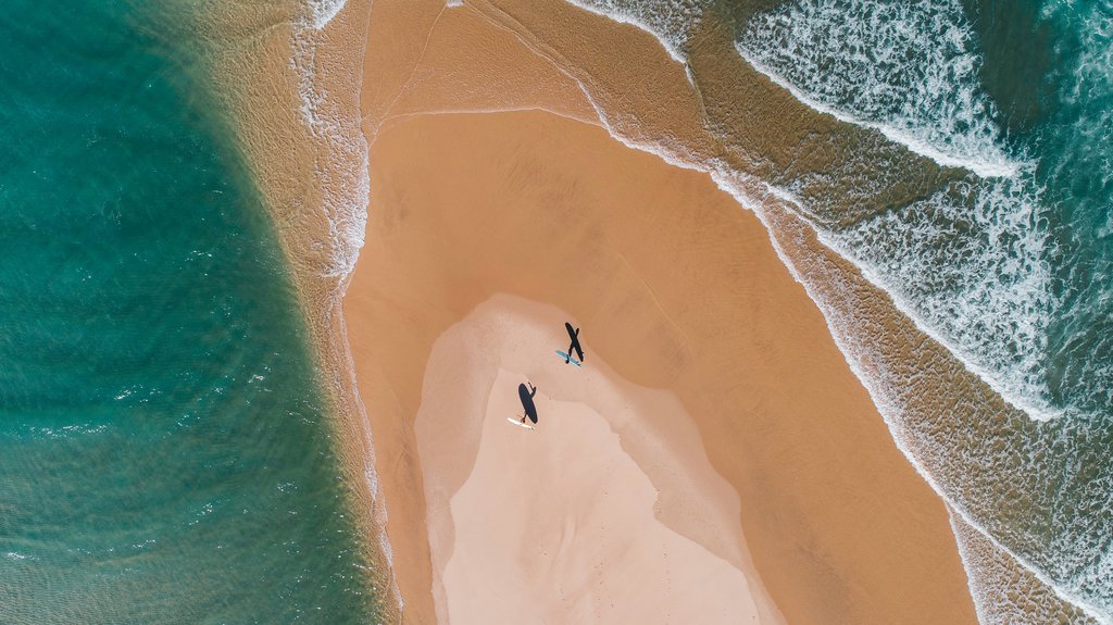 Zwei Surfer laufen auf einer Sandbank ins Meer