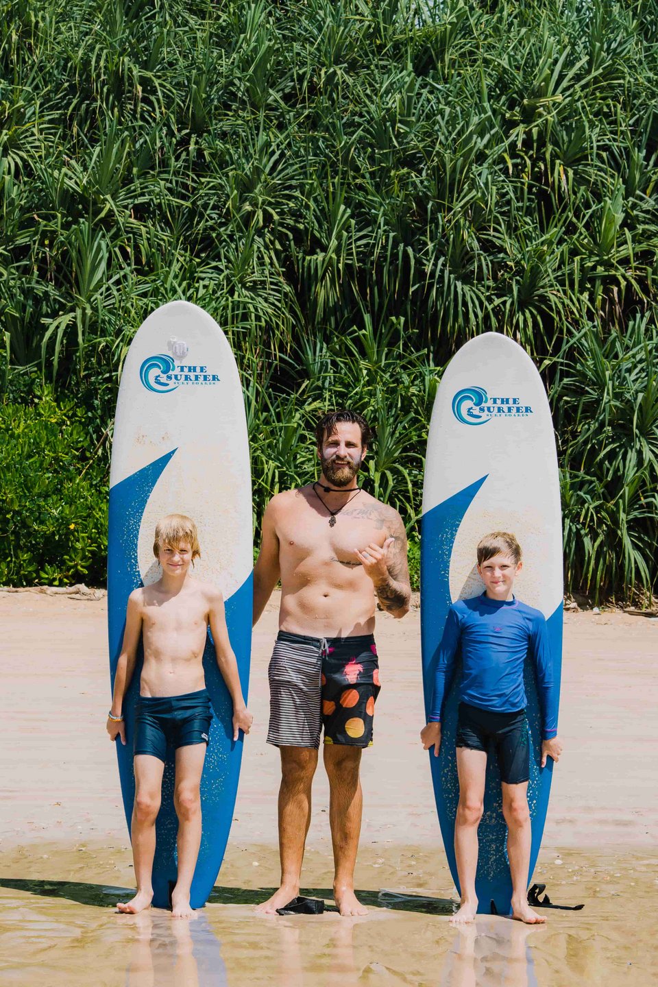 Surflehrer mit zwei glücklichen Kindern und ihren Boards am Strand
